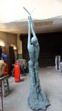 Back view of bronze sculpture Speak to us of Freedom. Tall, slim woman with hands stretching upwards with the Dove of Peace.