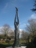 Speak to us of Freedom bronze sculpture. A tall, slim lady, releasing a Dove of Peace from hands held high. Blue sky.