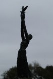 Silhouette of bronze sculpture Speak to us of Freedom. Tall, slim woman, hands stretching upwards with Dove of Peace.