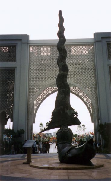 Bronze dagger sculpture with ceremonial arch behind, all flags flying for grand ceremonial. View away from stadium down pool.