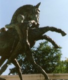 Photo of bronze prancing horse sculpture being restrained by two naked men, one each side, gripping the halter. Verdigris patina.
