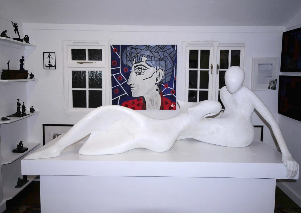 A resin version of the sculpture I Wish, finished to look like marble. Behind is a painting of Neil's wife Grace, with windows either side and shelves full of bronze maquettes on the left wall.