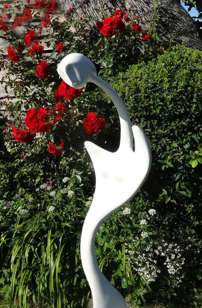 Emily - abstract sculpture in white resin in front of a bush of red roses