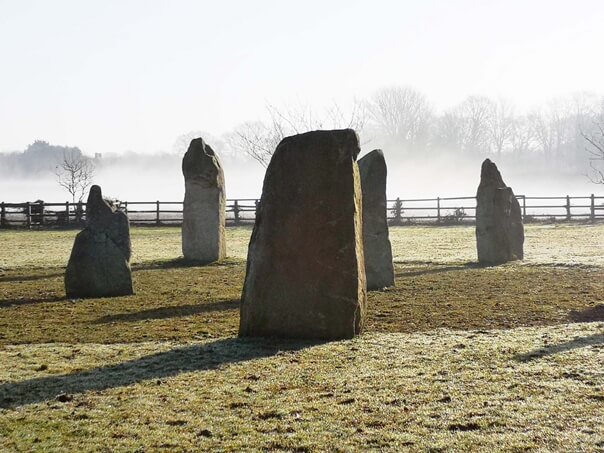 The Sussex Stone Circle. Five Standing Stones. Part of a circle. 3 on the edge and 2 in centre. Fence behind low mist beyond.