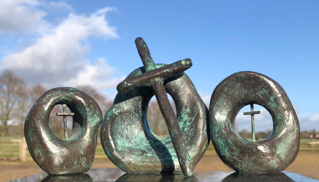 Easter. Bronze maquette. Three upright caves in row, edges touching. Middle has large cross outside. Others small one inside.