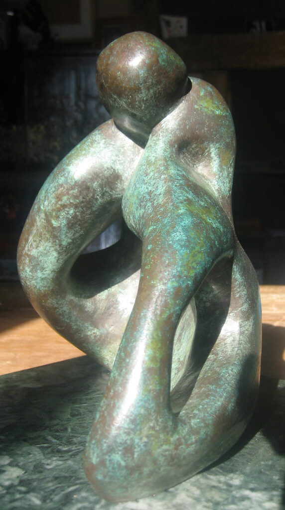 Closeup of abstract bronze sculpture of couple sitting on the ground kissing from the Gibran Sculpture Series. Marble plinth.