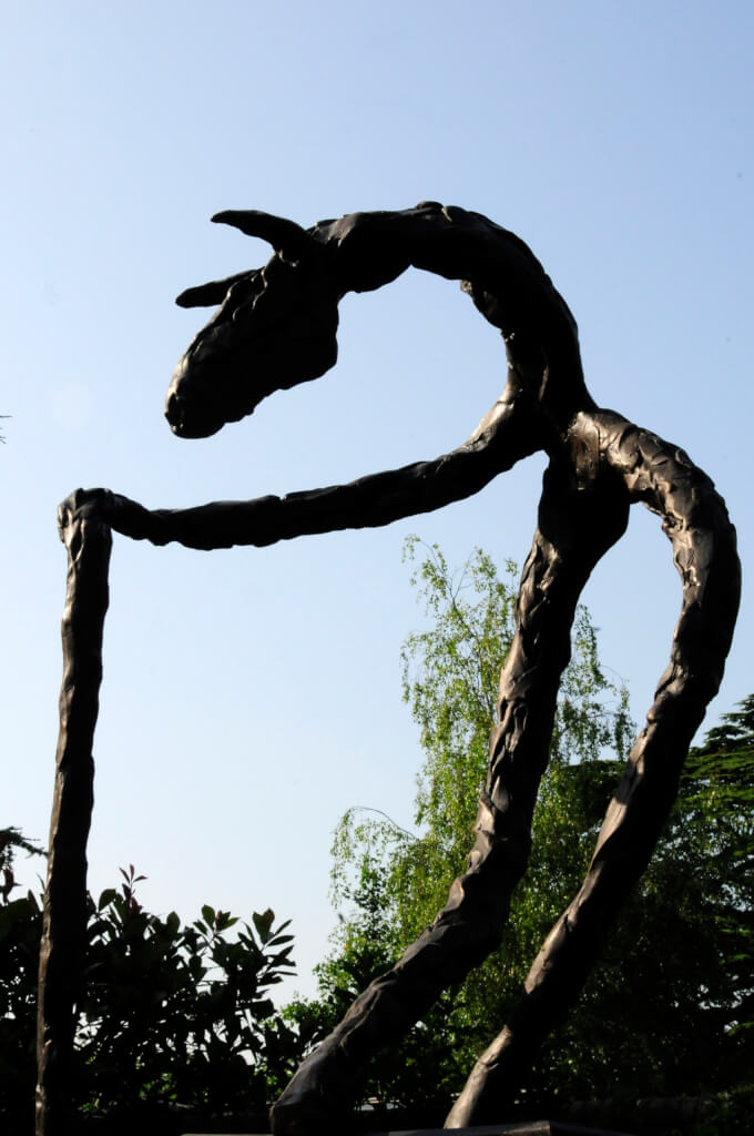 Bronze sculpture. A horse with a long neck, standing vertical on its hind legs, a single front leg holding a walking stick.