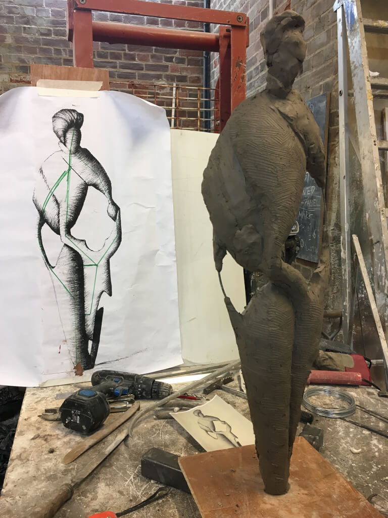 Photo of nearly complete clay model made from drawing on an easel behind,
