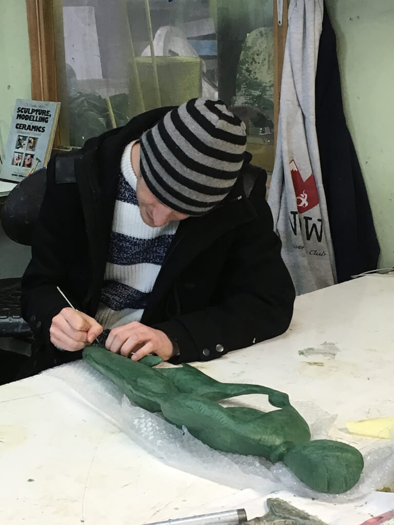 Artist signing a green clay sculpture model