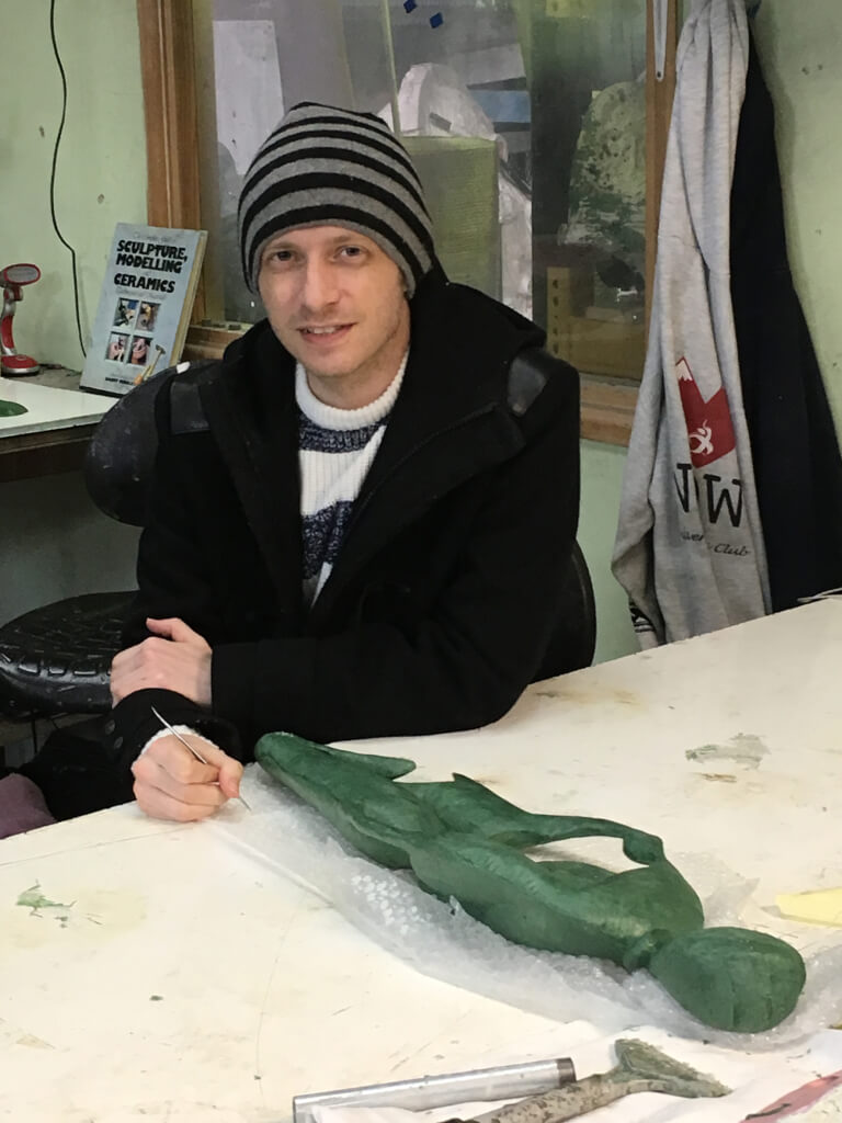 Greg sitting with the model lying flat in front of him on the workbench.